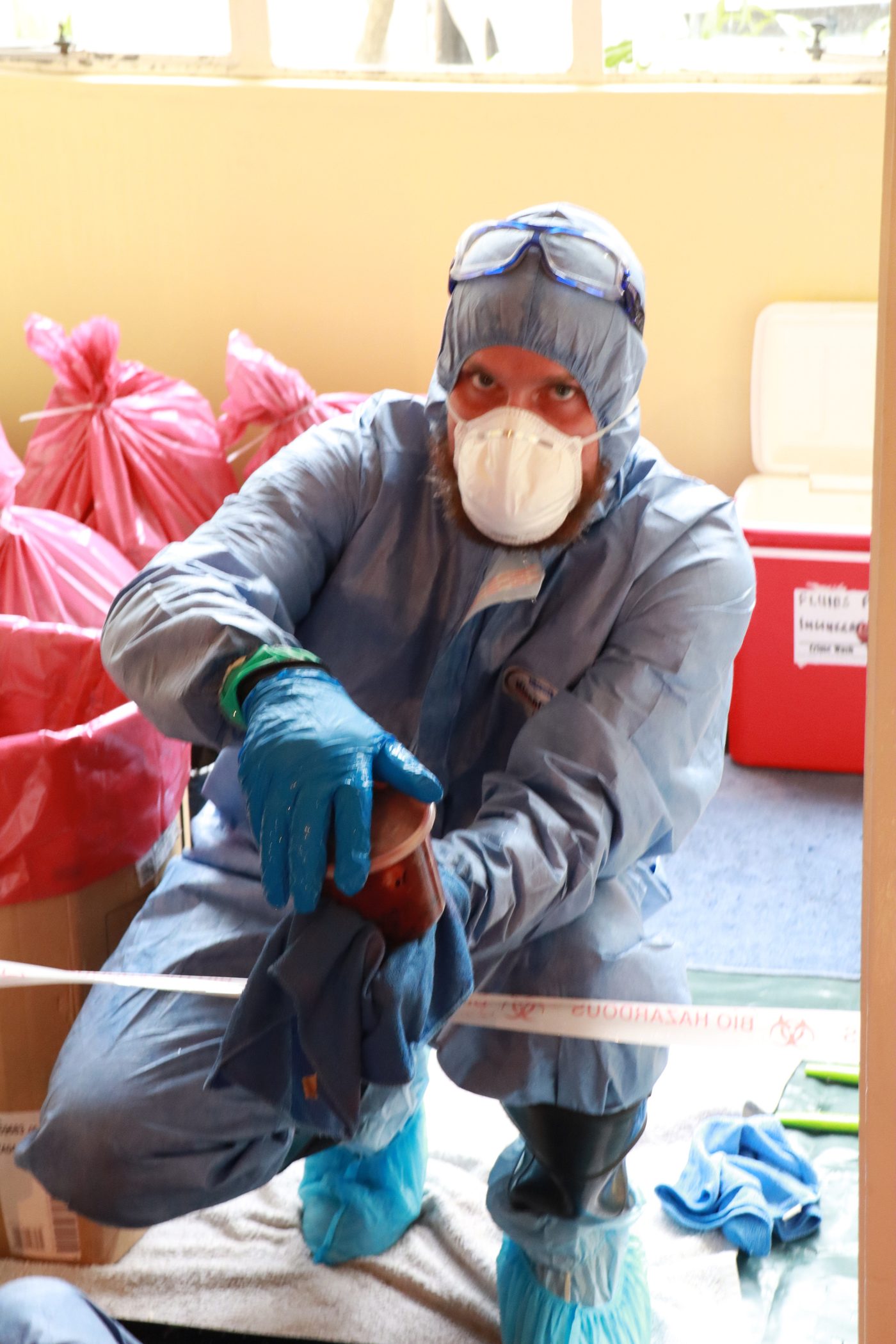 A Trauma Cleansing technician in protective equipment carefully handling biohazard waste